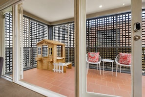 A balcony with a wooden playhouse, two white chairs with red cushions, and a metal gate. - Urban Hideaway in Carlton by Ready Set Stay (Carlton)