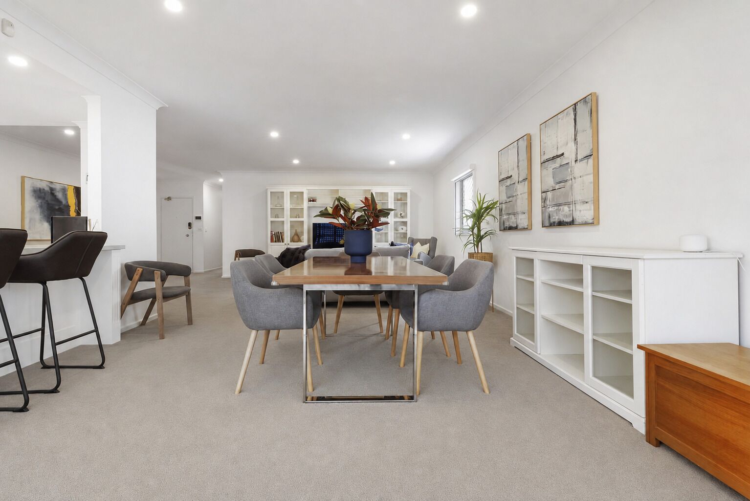 Un espace repas moderne avec une table centrale, des chaises grises et un meuble blanc doté de portes en verre.