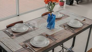 A dining table set with white plates, silverware, and a blue vase with orange flowers.