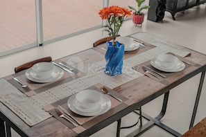 A dining table set with white plates, silverware, and a blue vase with orange flowers.