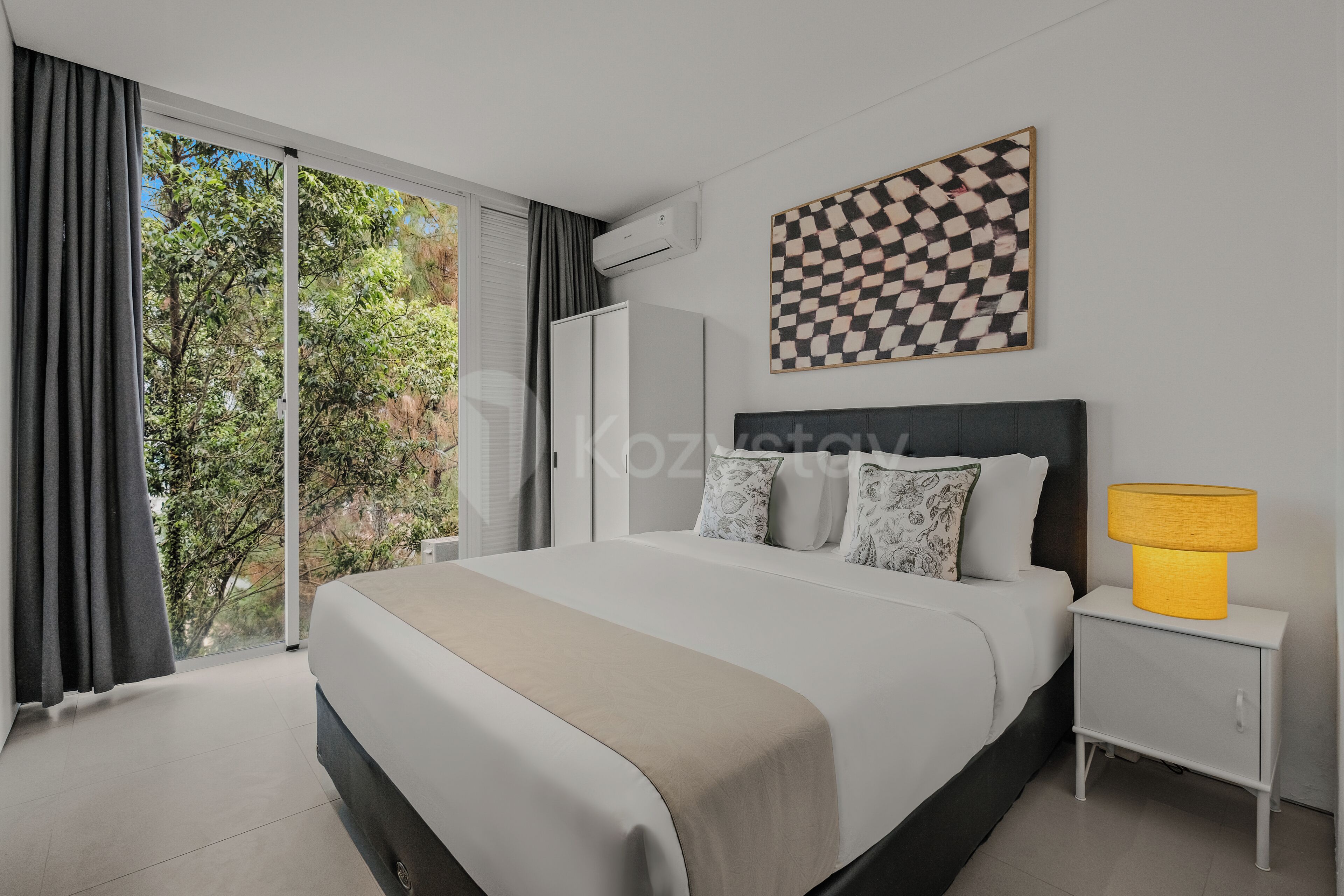 Un dormitorio moderno con una cama grande, una mesita de noche con lámpara y un cuadro de pared con diseño escocés.