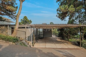 A covered outdoor area with a concrete floor, metal railing, and a view of a residential building.