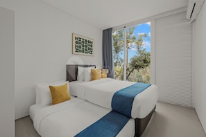 A modern hotel room with a bed, two bedside tables, a window with a view of trees, and a wall-mounted artwork.