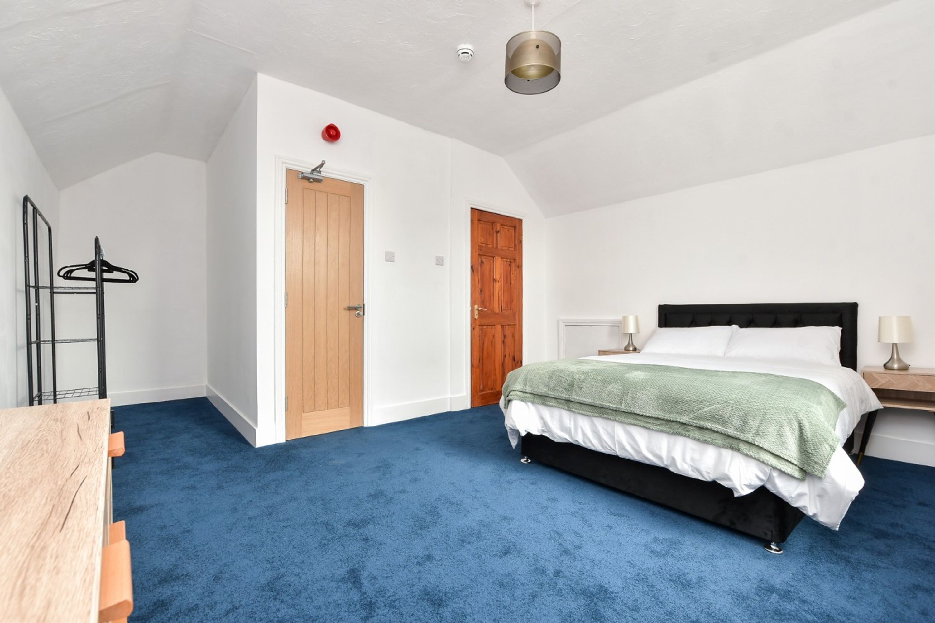 A bedroom with a bed, a wooden door, a coat rack, and a hanging light fixture.