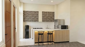 A compact kitchen with a central island, two bar stools, a refrigerator, a microwave, and a water dispenser. - Arunava Stay by Sinergi (Semarang)