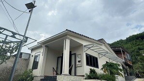 A two-story house with a covered porch, a staircase leading to the entrance, and a solar panel on the roof.