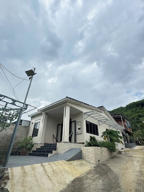 A two-story house with a covered porch, a staircase leading to the entrance, and a solar panel on the roof. - Lộc Rừng Hill (Dien Tho)