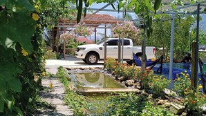 A garden pathway with a white pickup truck parked on the side, surrounded by lush greenery and flowering plants.