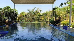 A swimming pool with a covered area, surrounded by lush greenery and a hammock.