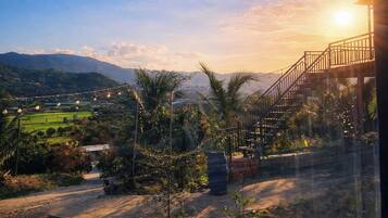 Une vue sur le coucher de soleil depuis un balcon avec un escalier, un jardin avec différentes plantes et un paysage lointain.
