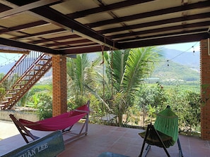 A covered outdoor area with a hammock, a swing, and a view of a mountainous landscape. - Lộc Rừng Hill (Dien Tho)