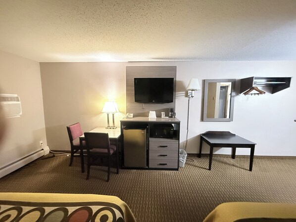 A hotel room with a desk, chairs, a television, a lamp, a mirror, and a bed.