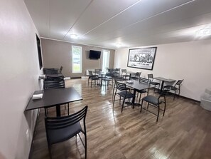 A conference room with multiple tables and chairs, a flat-screen TV mounted on the wall, and a framed picture of a lake.