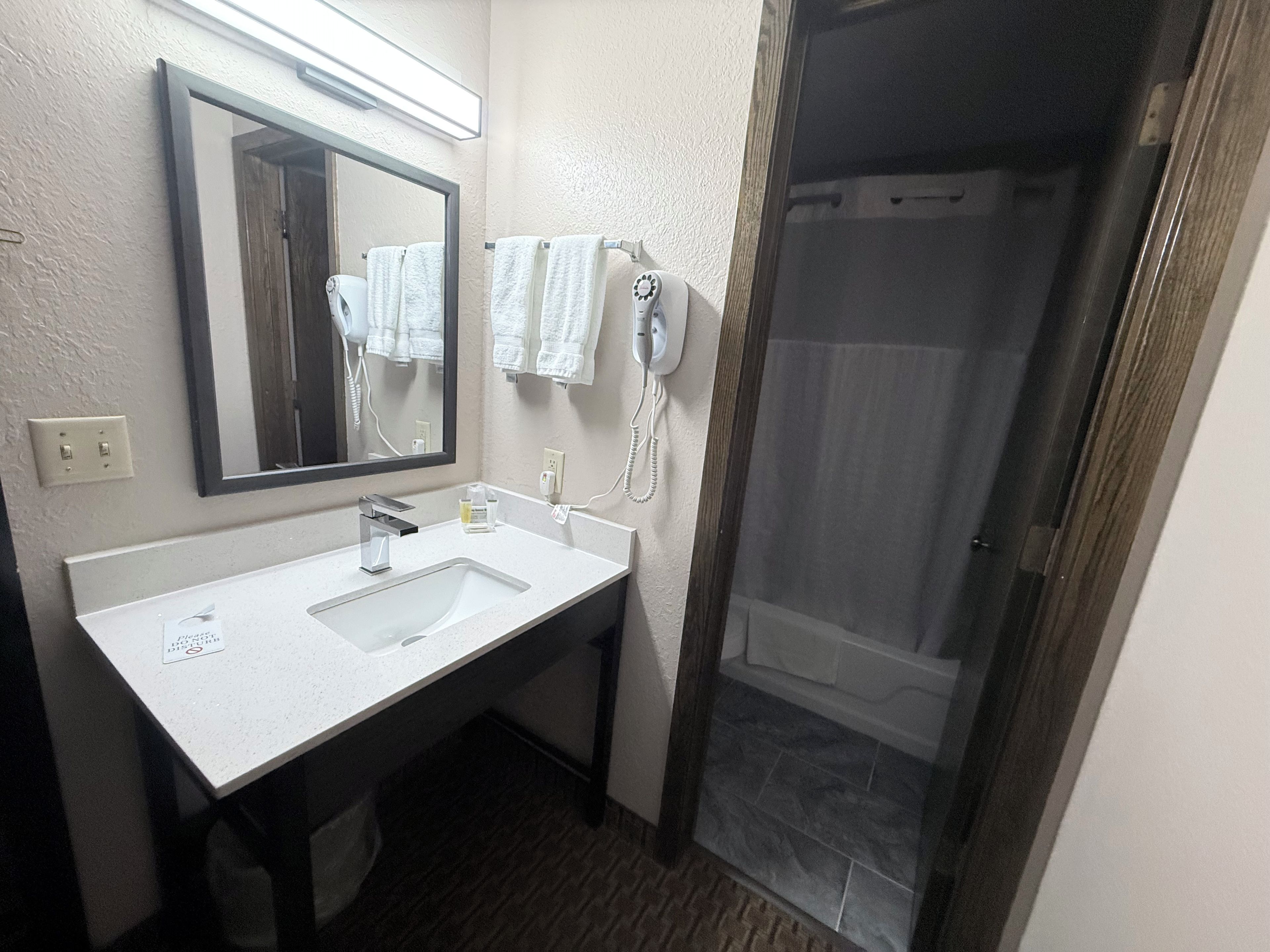 A bathroom with a white sink, a mirror, a hairdryer, and a shower area.