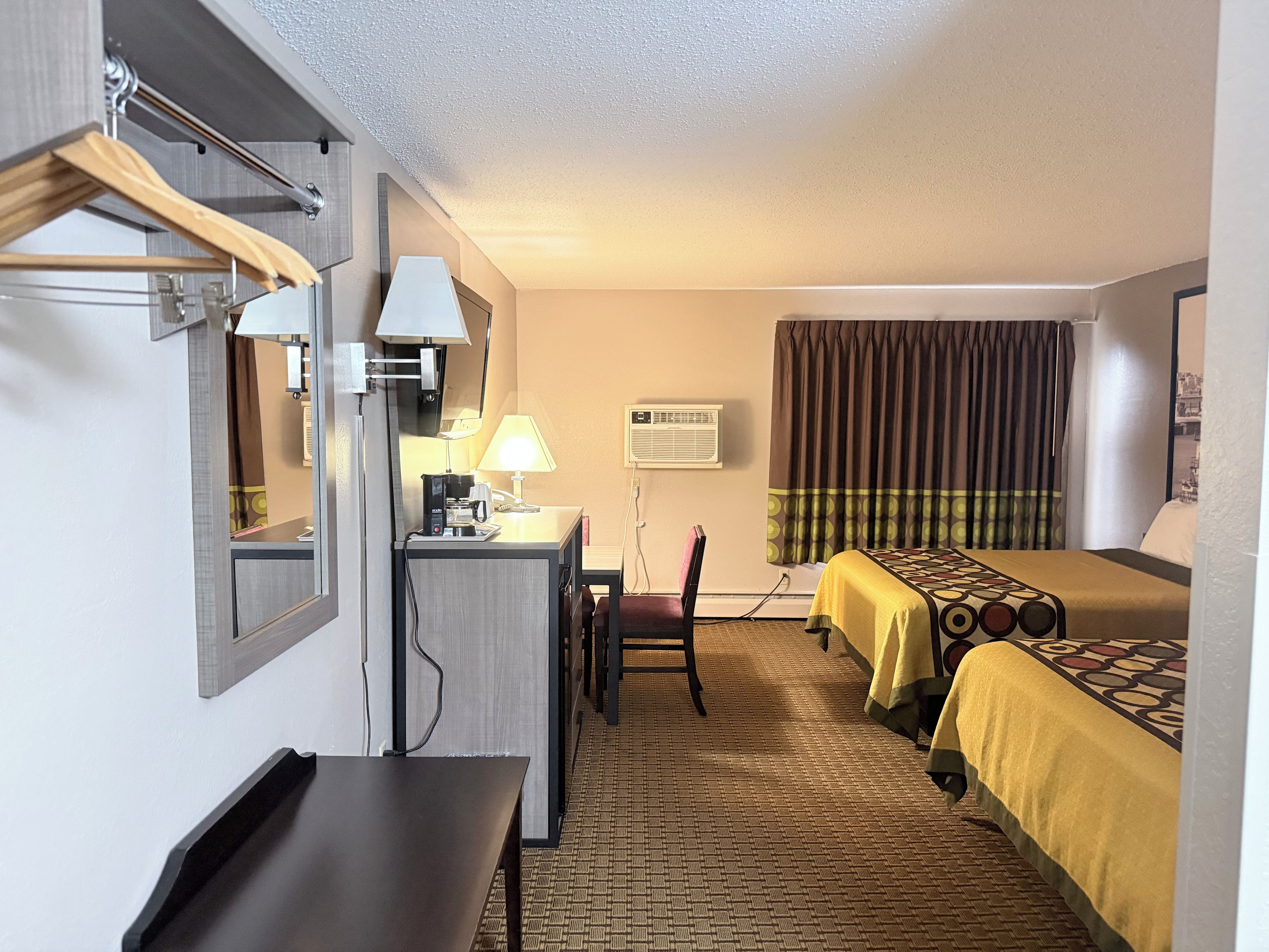 Une chambre d’hôtel équipée d’un bureau, d’une chaise, d’un lit et d’une fenêtre avec des rideaux.