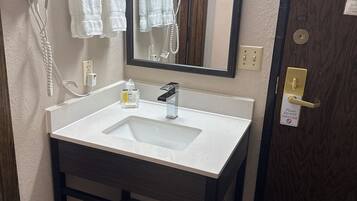 A bathroom with a white sink, a mirror, a hairdryer, and a towel rack.