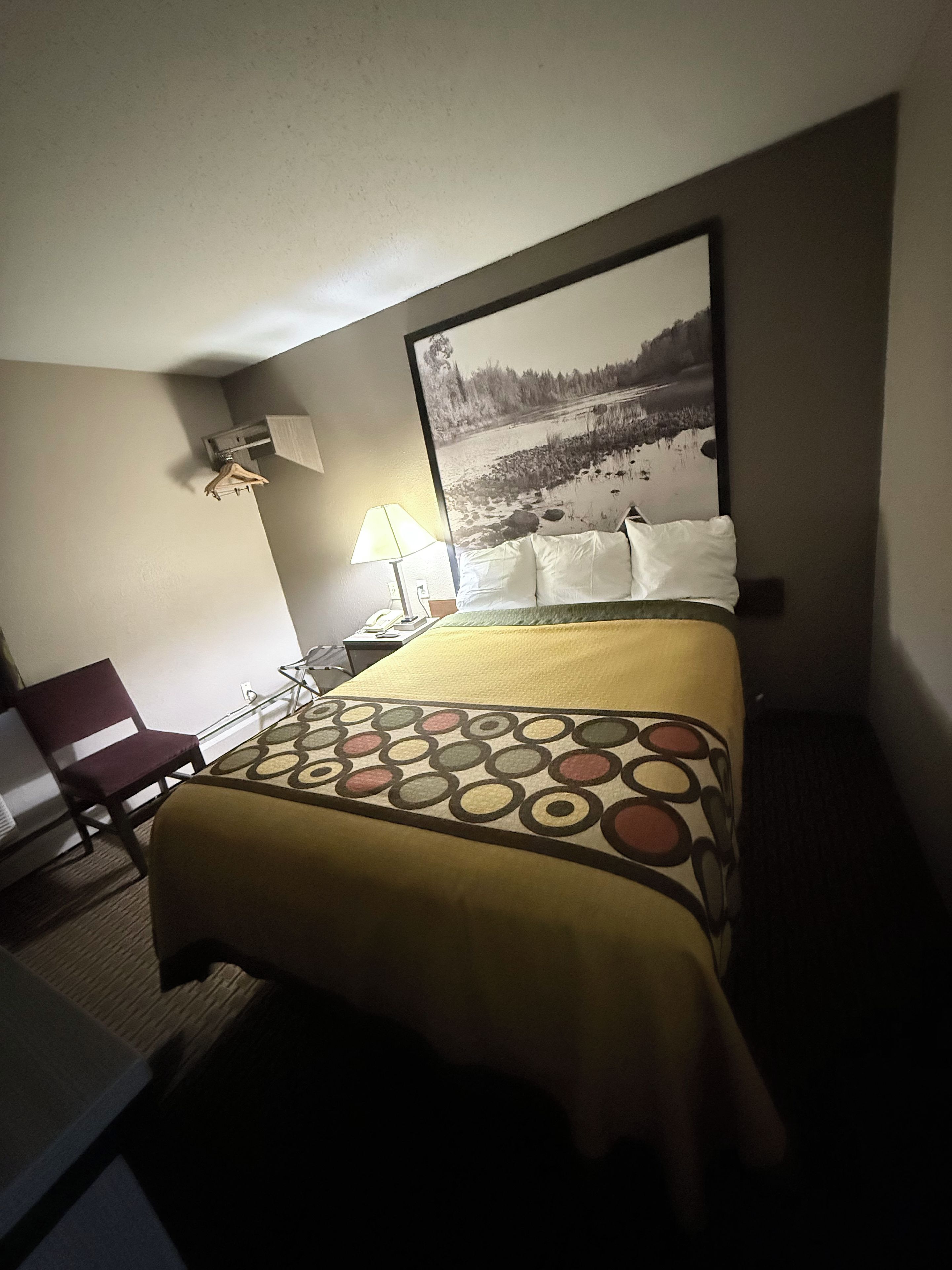 A hotel room with a bed, a chair, a lamp, and a painting on the wall.