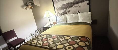 A hotel room with a bed, a chair, a lamp, and a painting on the wall.