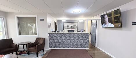 A reception area with a counter, chairs, a rug, and a television screen.
