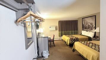 Quarto de hotel com cama, escrivaninha, cadeira, cabideiro e janela com cortinas.