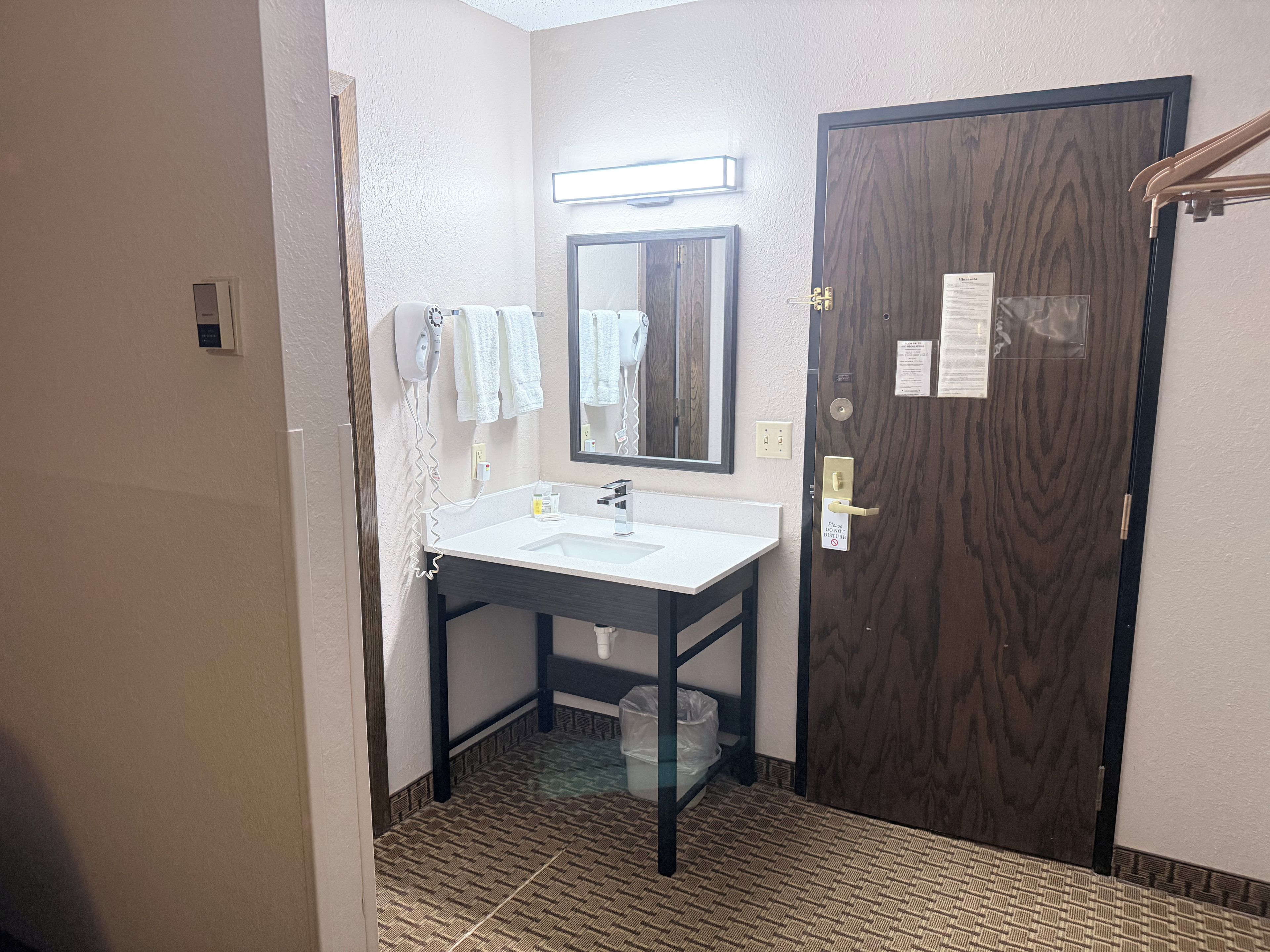 A bathroom with a white sink, a mirror, a towel rack, and a wooden door.