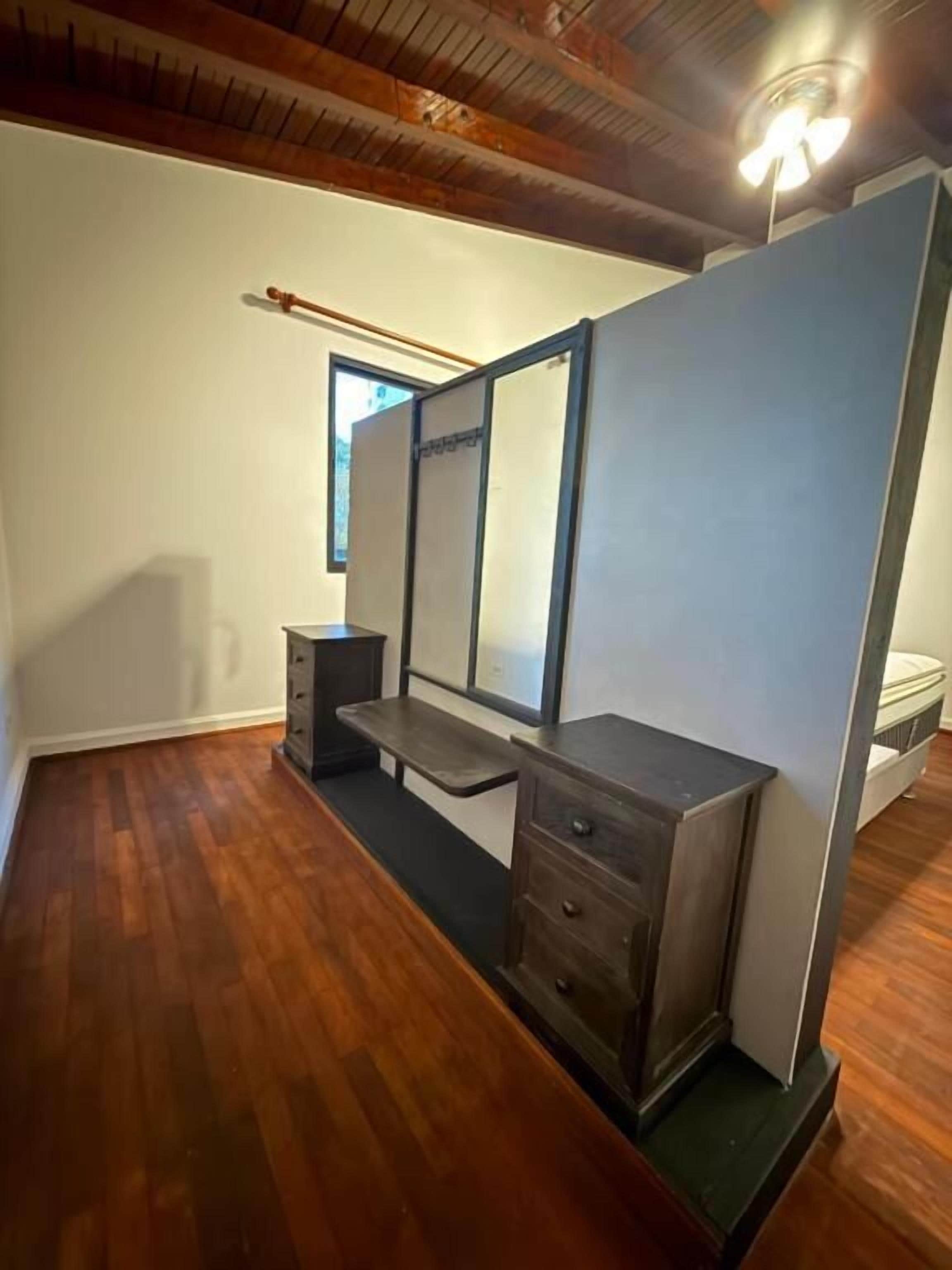 A room with a wooden floor, a bench, a dresser, and a large mirror.