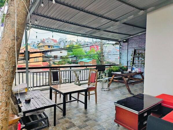 A covered outdoor seating area with tables and chairs, a laptop, and a red sofa. - BIKA Farmstay and Camping (Xuan Truong - Da Lat)