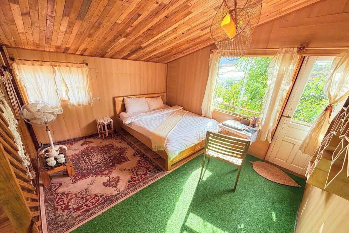 A wooden room with a bed, a fan, a chair, and a window.