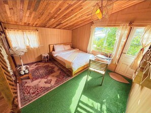 A wooden room with a bed, a fan, a chair, and a window. - BIKA Farmstay and Camping (Xuan Truong - Da Lat)