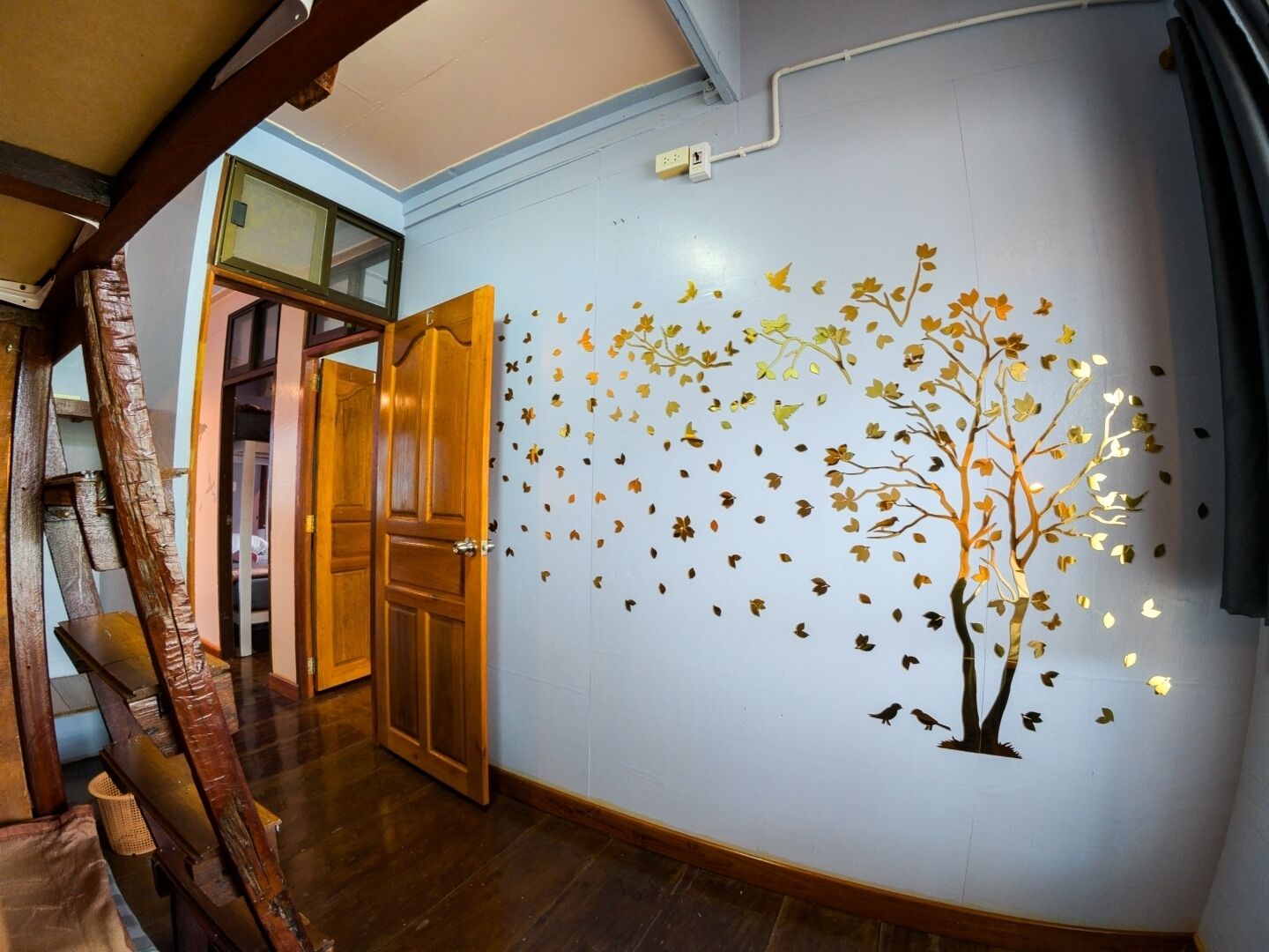 A hallway with a wooden door, a wall with a tree and leaves decal, and a visible electrical outlet.