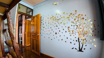 A hallway with a wooden door, a wall with a tree and leaves decal, and a visible electrical outlet.