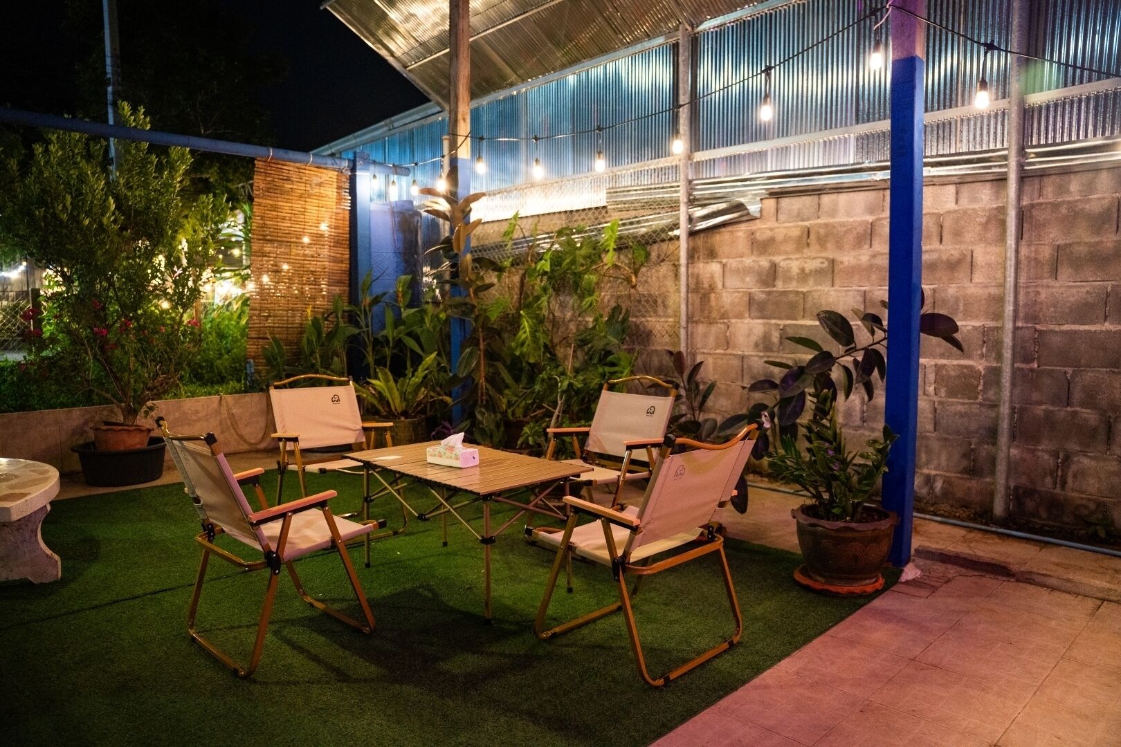 An outdoor patio with a table and chairs, surrounded by potted plants and a brick wall.