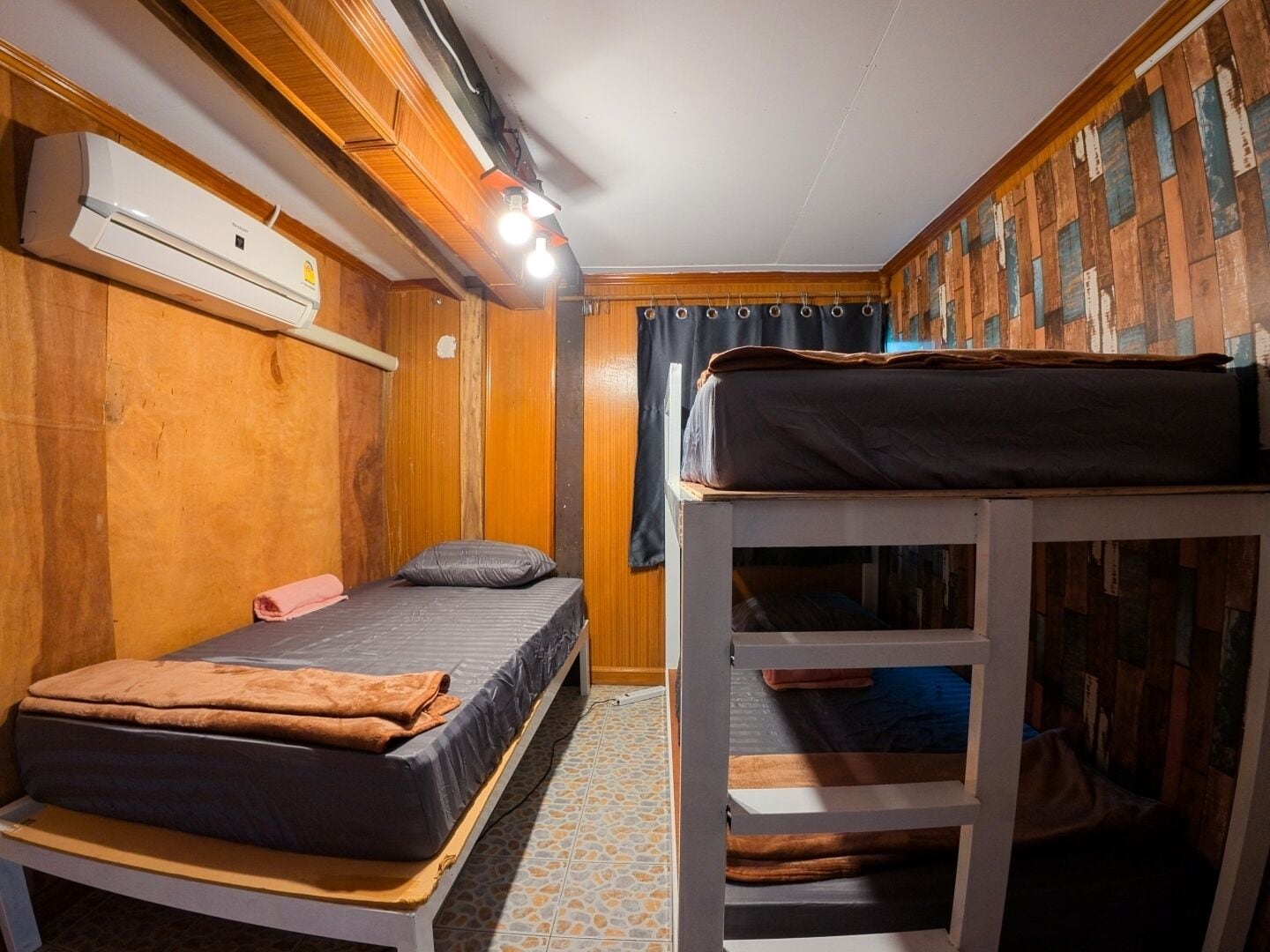 A compact room with a bunk bed, a single bed, and a built-in air conditioning unit.