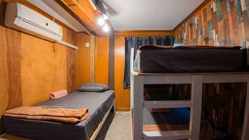 A compact room with a bunk bed, a single bed, and a built-in air conditioning unit.