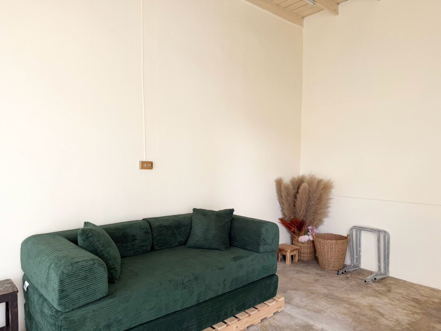 A green sofa in a room with a white wall, a wooden floor, and a small wooden stool.