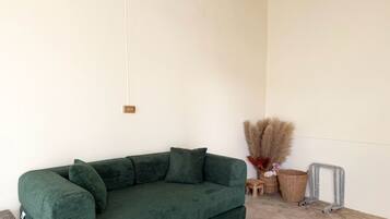 A green sofa in a room with a white wall, a wooden floor, and a small wooden stool.