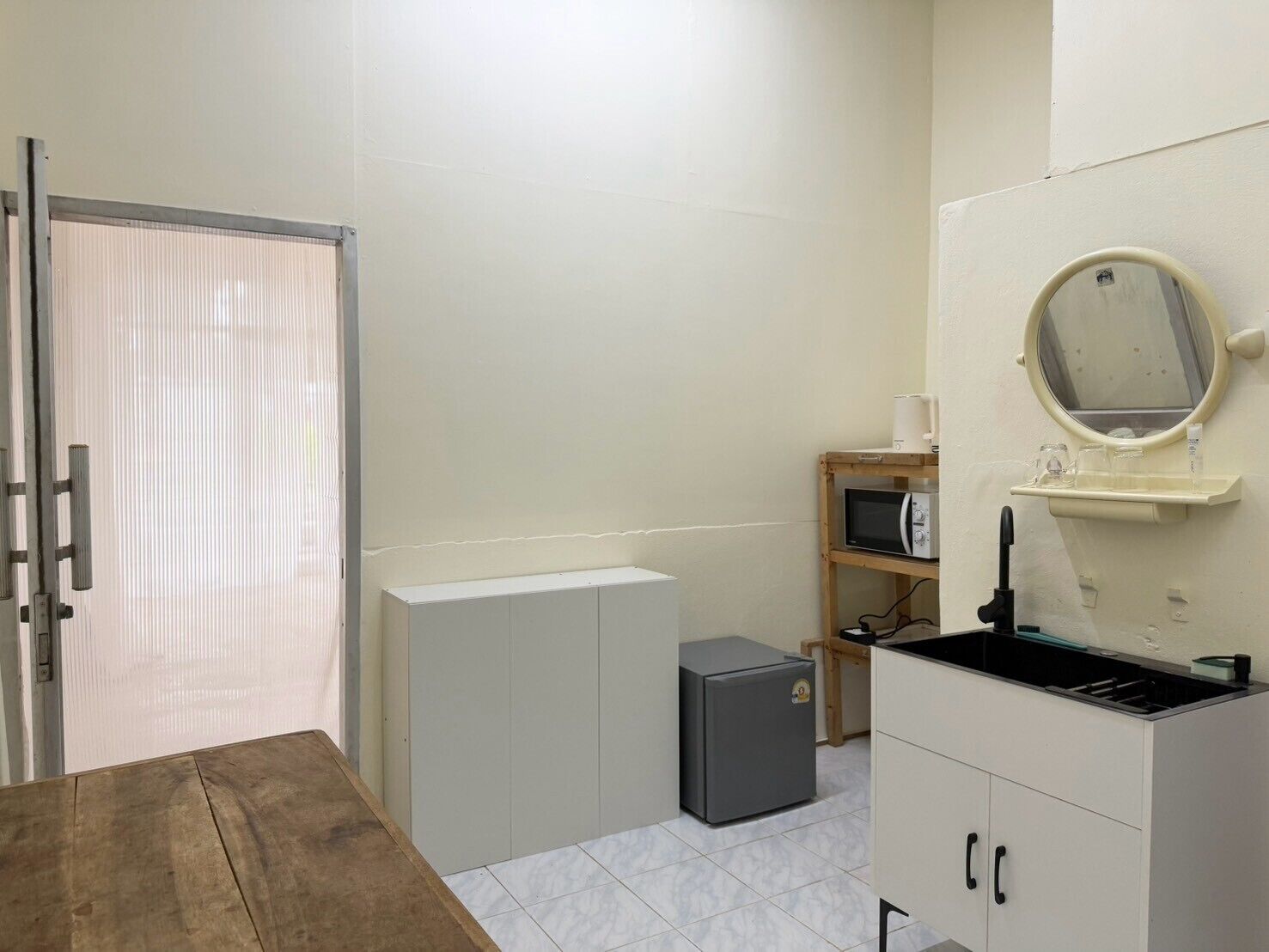 A compact kitchenette with a microwave, a small refrigerator, and a sink with a mirror above it.