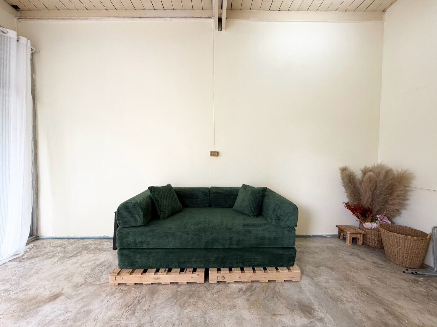 A green sofa on a wooden pallet in a room with white walls and a concrete floor.