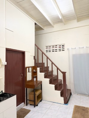 Una escalera con escalones de madera y barandilla, una puerta marrón y una pared blanca con un ventanal pequeño.