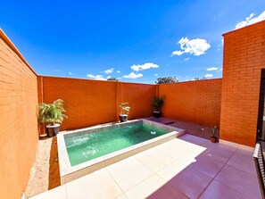 A rectangular swimming pool with a tiled deck, surrounded by a brick wall and potted plants.