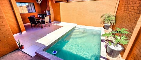 Una piscina rectangular con borde de baldosas, rodeada de muros de ladrillo y plantas en macetas.