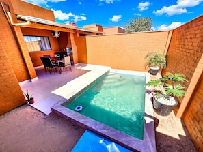 A rectangular swimming pool with a tiled deck, surrounded by brick walls and potted plants. - Vacation home with 2 bedrooms and pool - Caldas Novas (Caldas Novas)