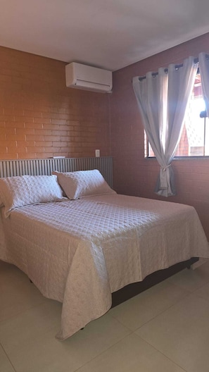 Ein Zimmer mit einem Einzelbett, einer Ziegelwand, einem Fenster mit Vorhängen und einer Klimaanlage.