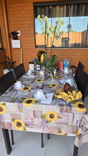 A dining table with a sunflower tablecloth, a vase with flowers, and a fruit bowl. - Vacation home with 2 bedrooms and pool - Caldas Novas (Caldas Novas)