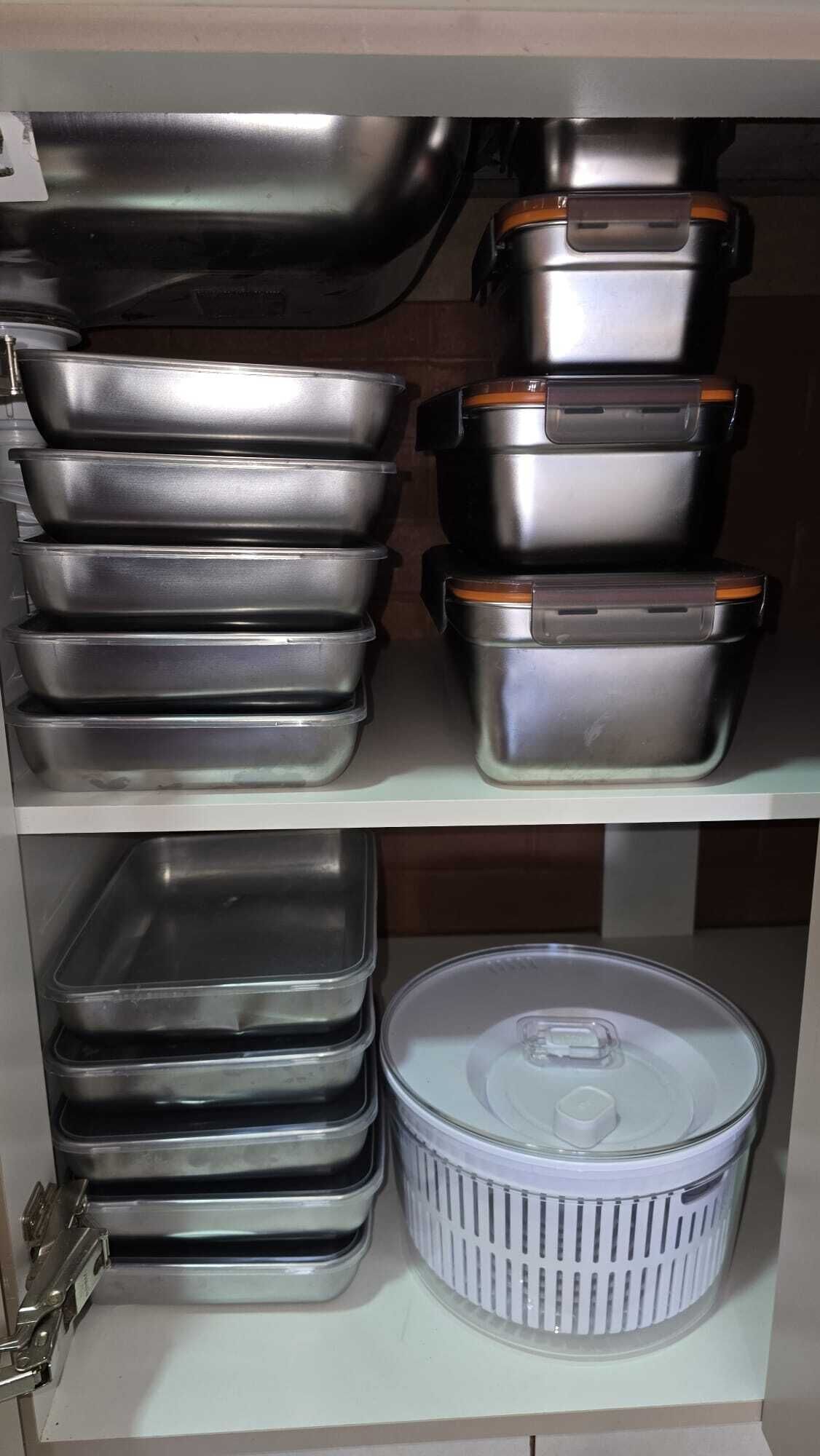 A kitchen shelf with stainless steel cookware and a plastic container.