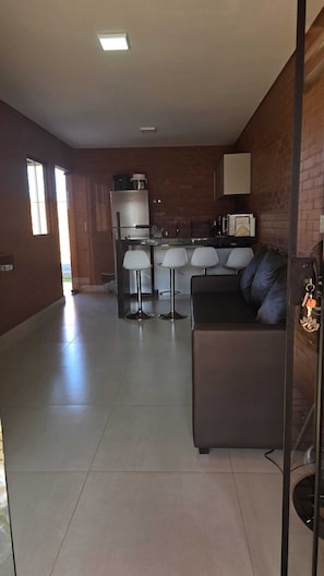 Eine moderne Küche mit Kühlschrank, Mikrowelle und Kaffeemaschine. Ein Essbereich mit Tisch und Stühlen ist vorhanden. Der Raum verfügt über ein großes Fenster und eine Couch.