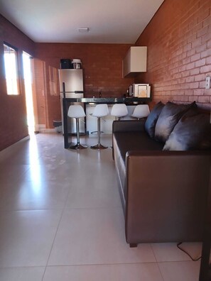 A modern living area with a sofa, a coffee table, and a kitchen area with a counter and stools.