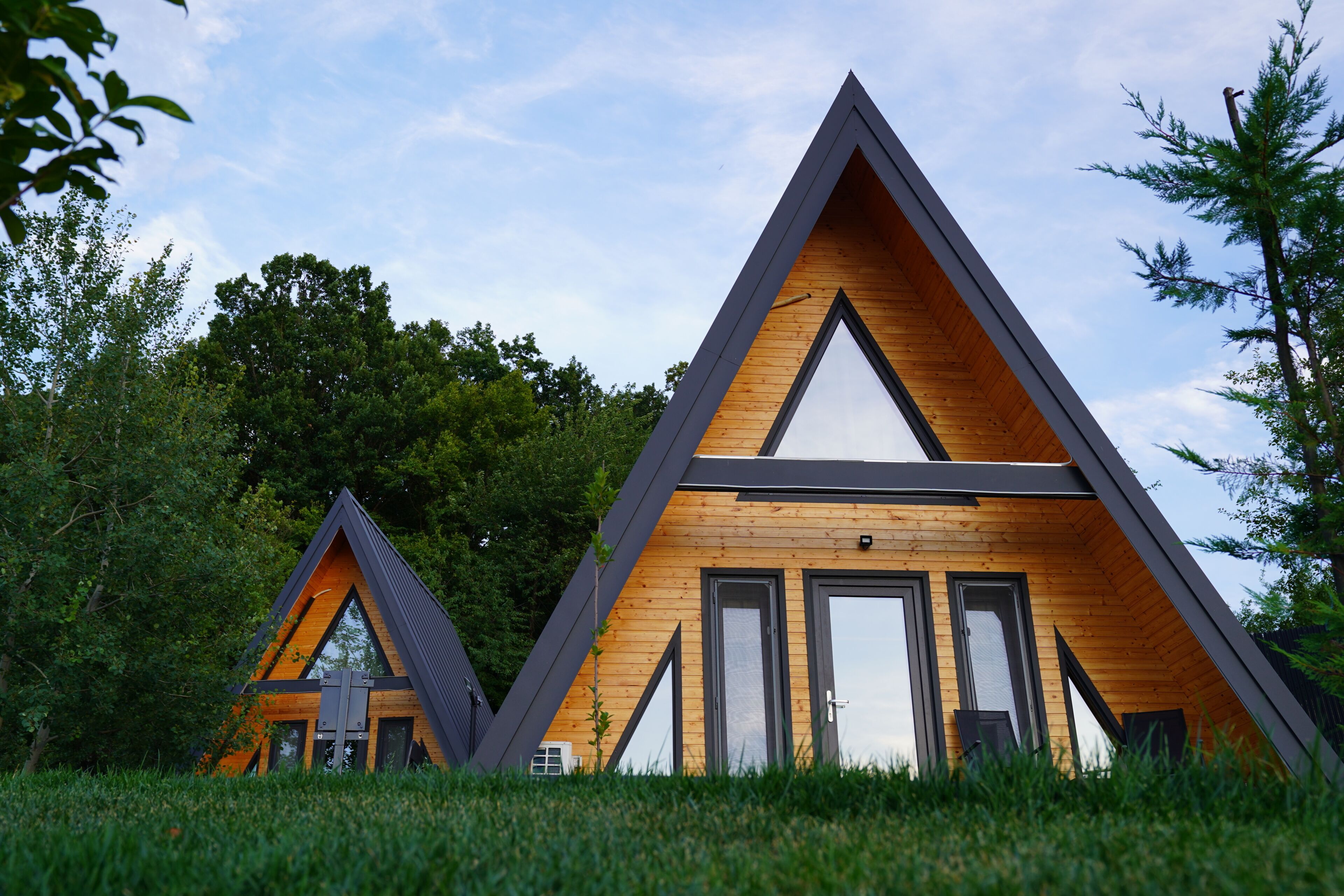 Deux cabanes triangulaires en bois, dotées de grandes fenêtres et surplombant un pré verdoyant.