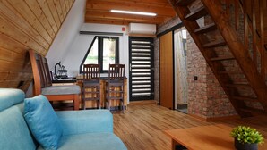 A cozy loft bedroom with a sloped ceiling, wooden beams, a sofa, a dining table, and a staircase.