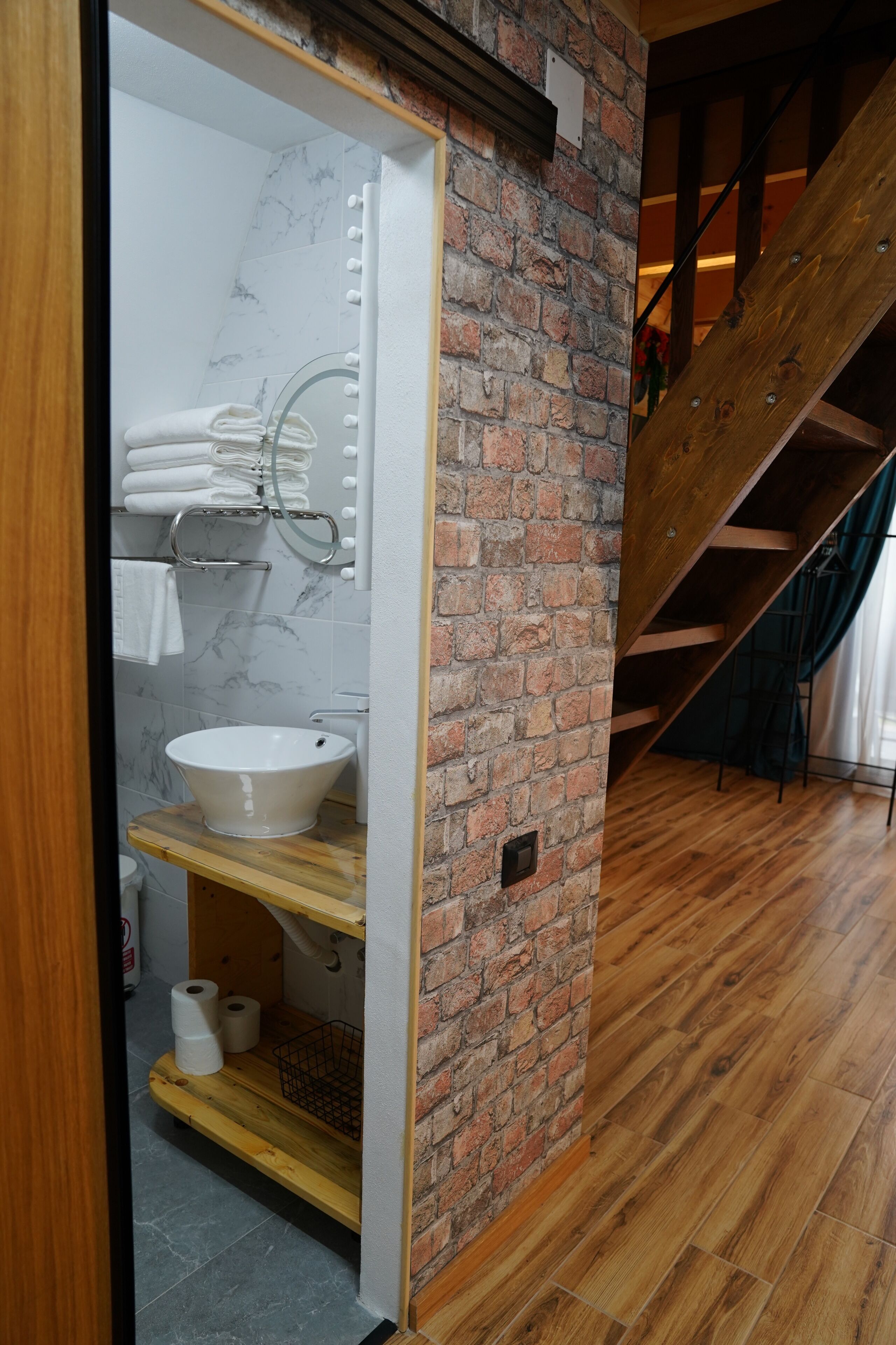 Une salle de bain avec un mur recouvert de carreaux de marbre, un lavabo blanc et un meuble-lavabo en bois.